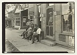 Men With Dog Sitting On Bench In Front Of General Store