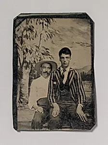 [Young Man in a Striped Jacket, Sitting on the Lap of Another Man in Front of Painted Outdoor Backdrop] by Unknown