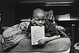 Margie's son, Jamont, 9, watches from his perch on a bunk bed as his mother chooses a dress for her job-training class. In the United States an alarming number of children are homeless. Olive Branch Mission, Chicago.