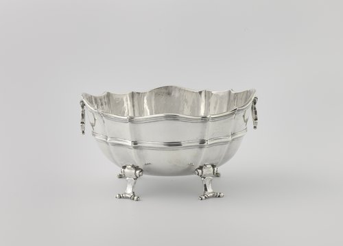 Sauskom van zilver, ovaal, op vier ingerolde pootjes. Filetranden langs de geschulpte bovenkant.